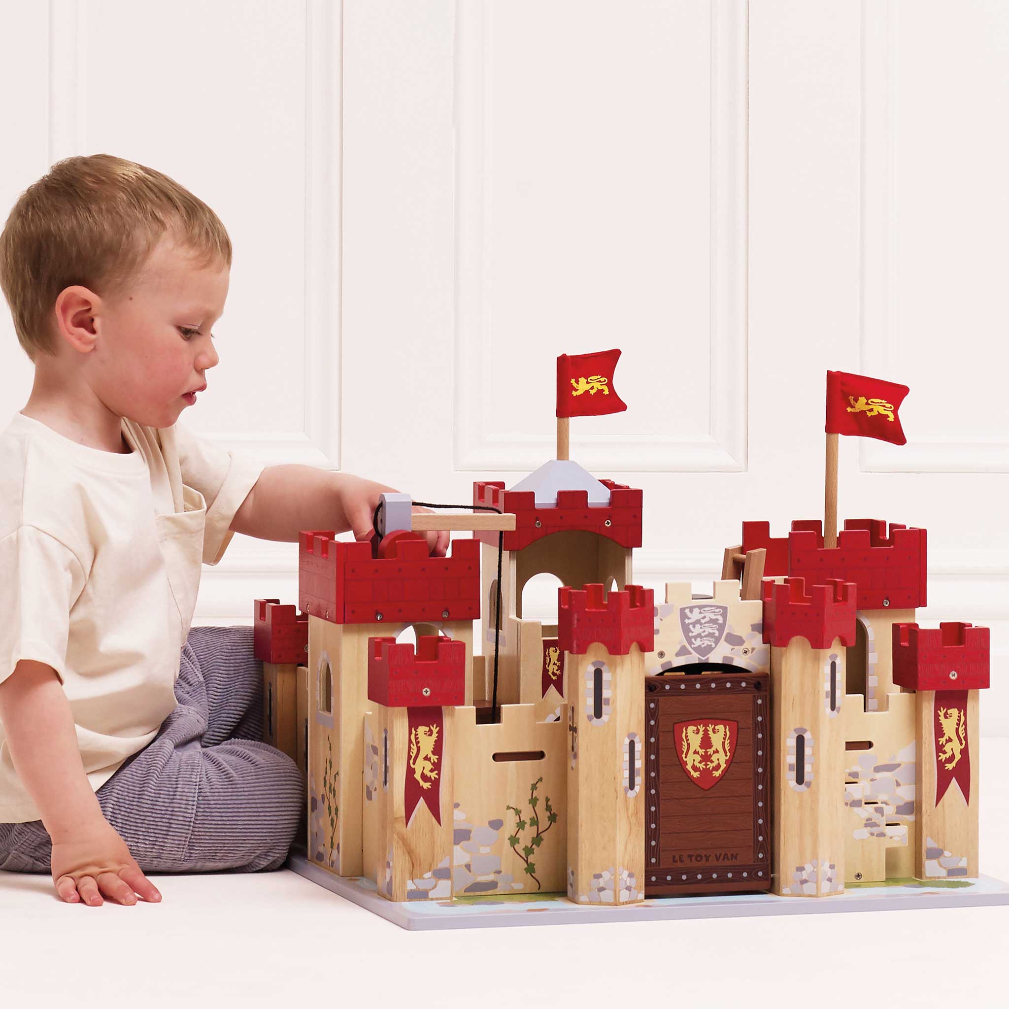 Child playing with a wooden toy castle set on a white surface.