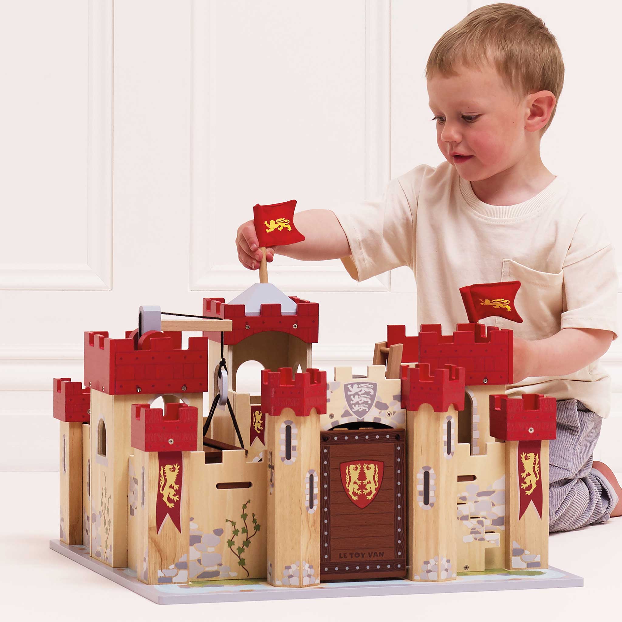 Child playing with a wooden castle toy set on a white background