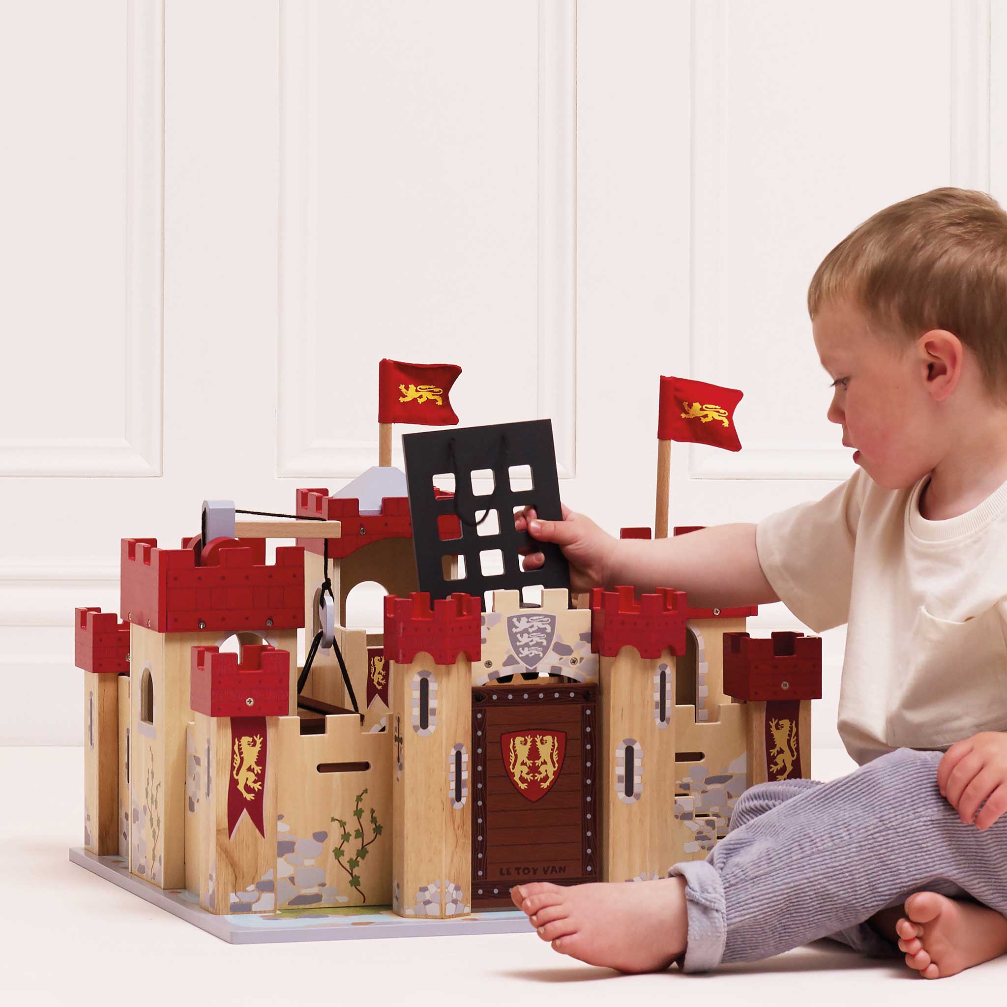 Child playing with a wooden toy castle on a white floor.