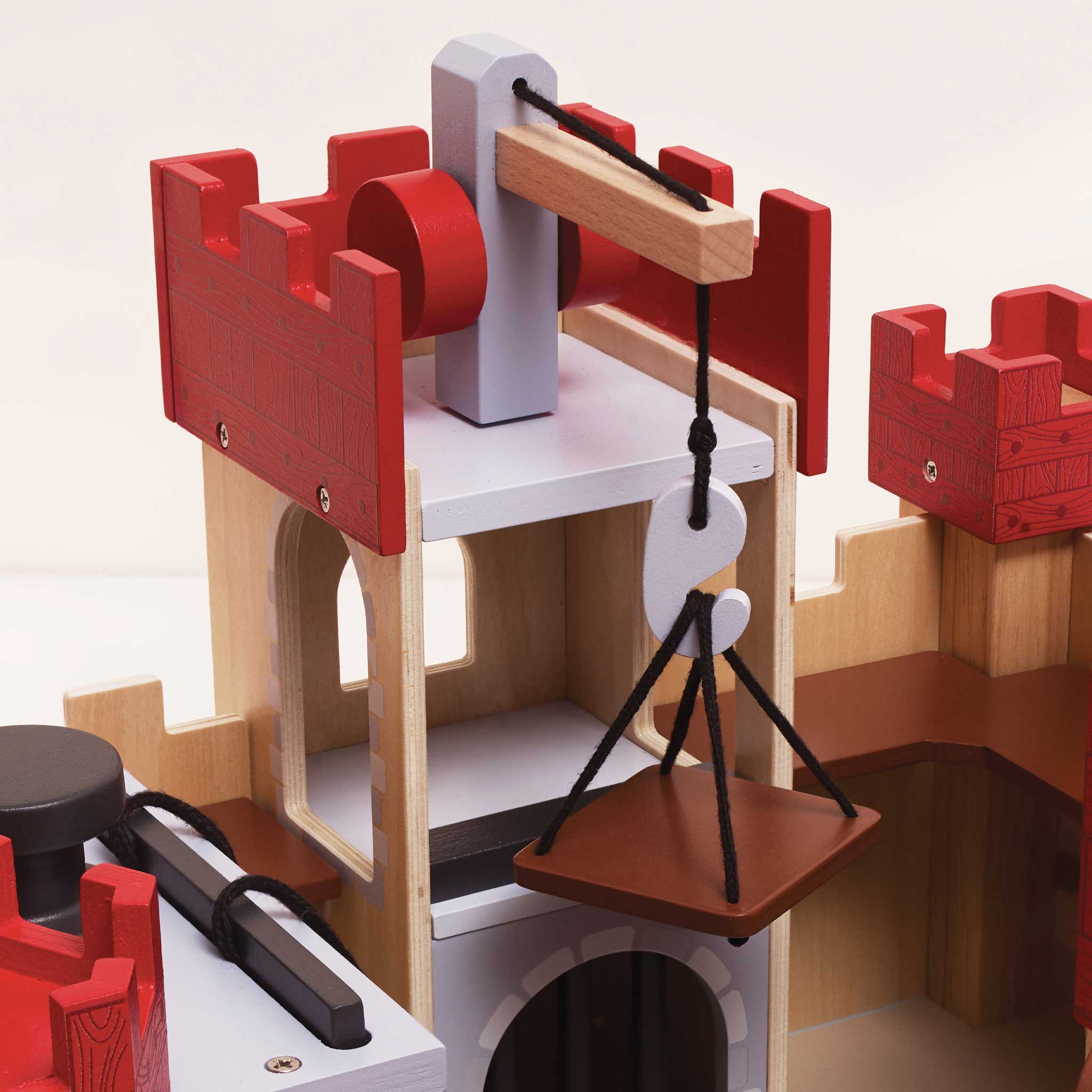 Wooden toy castle with red towers and a pulley system on a white background